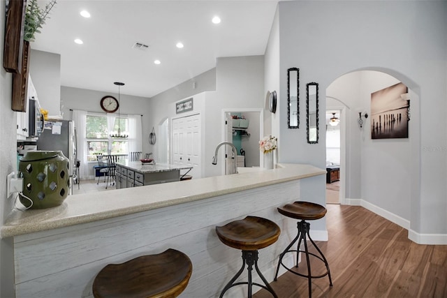 kitchen featuring light stone countertops, kitchen peninsula, light hardwood / wood-style floors, decorative light fixtures, and a kitchen island