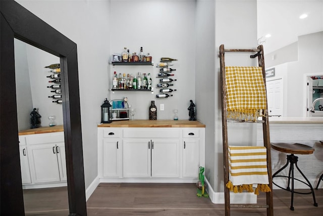 bar with butcher block counters, white cabinets, and dark wood-type flooring