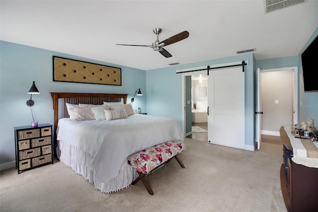 bedroom featuring a barn door, ceiling fan, ensuite bathroom, and light carpet