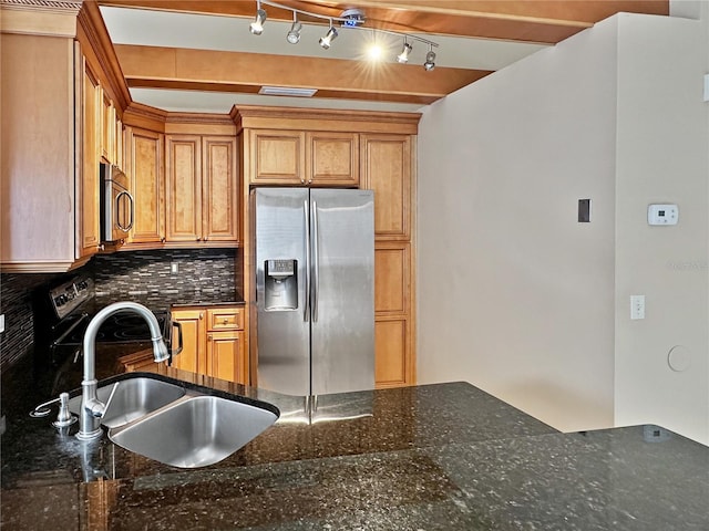 kitchen featuring appliances with stainless steel finishes, tasteful backsplash, track lighting, dark stone counters, and sink