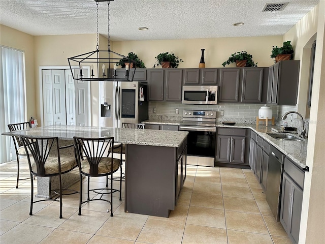 kitchen with pendant lighting, sink, appliances with stainless steel finishes, a center island, and light stone countertops