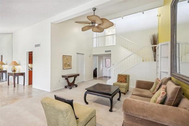 living room with beamed ceiling, ceiling fan, light colored carpet, and a high ceiling