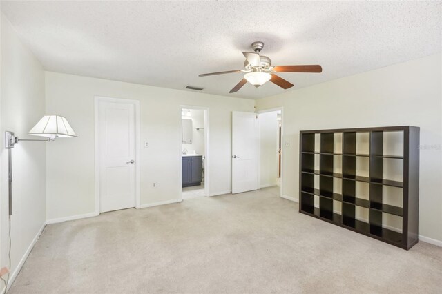 unfurnished bedroom with ensuite bathroom, light colored carpet, and a textured ceiling