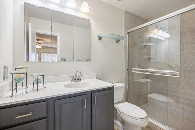 bathroom with vanity, toilet, ceiling fan, and a shower with shower door