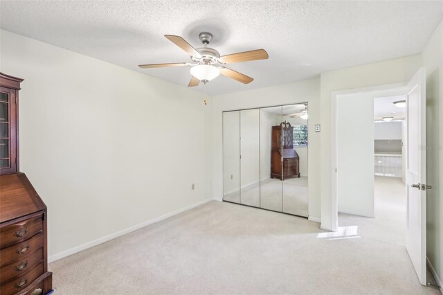 unfurnished bedroom with ceiling fan, light colored carpet, a textured ceiling, and a closet