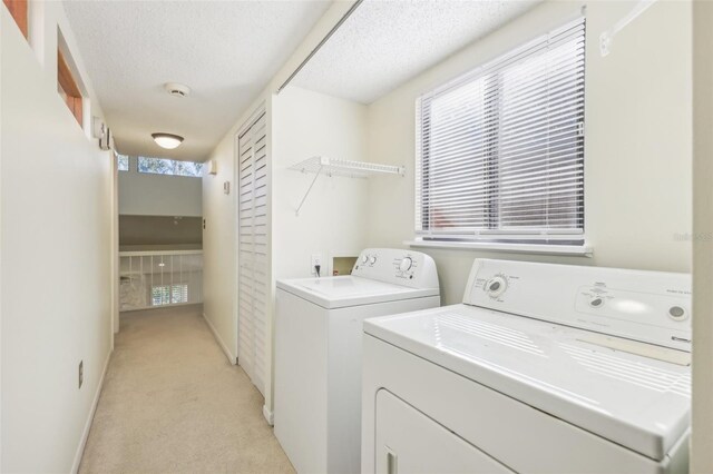 clothes washing area with light carpet, a textured ceiling, and separate washer and dryer