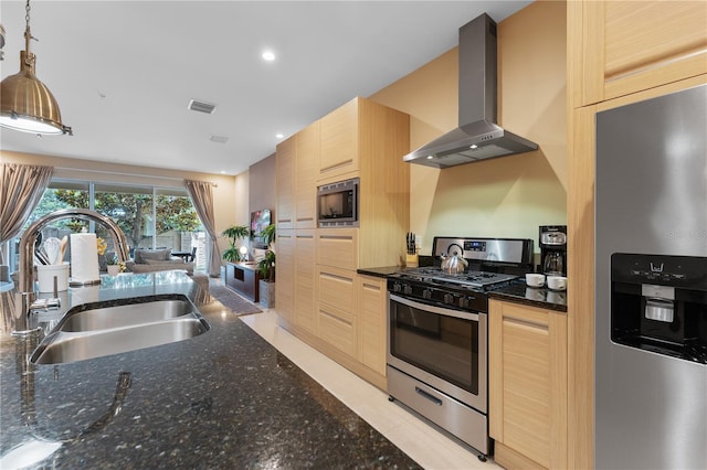 kitchen featuring sink, wall chimney range hood, light brown cabinets, appliances with stainless steel finishes, and decorative light fixtures