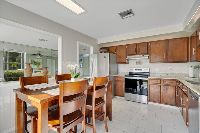 kitchen with ceiling fan, stainless steel appliances, light stone counters, and decorative backsplash