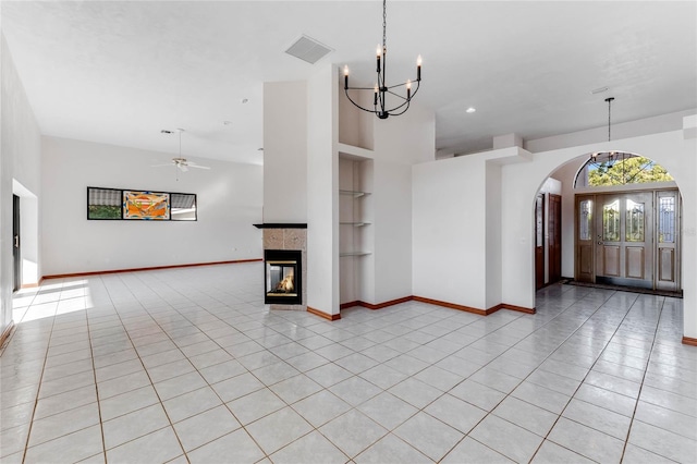 interior space with a tiled fireplace, ceiling fan with notable chandelier, built in features, and light tile patterned floors