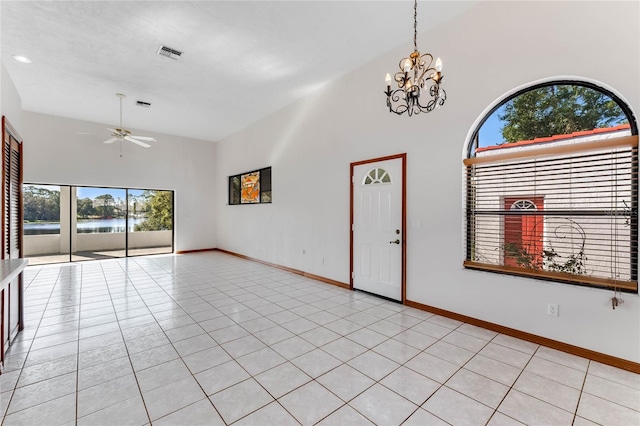 tiled empty room featuring a wealth of natural light, ceiling fan with notable chandelier, a water view, and high vaulted ceiling