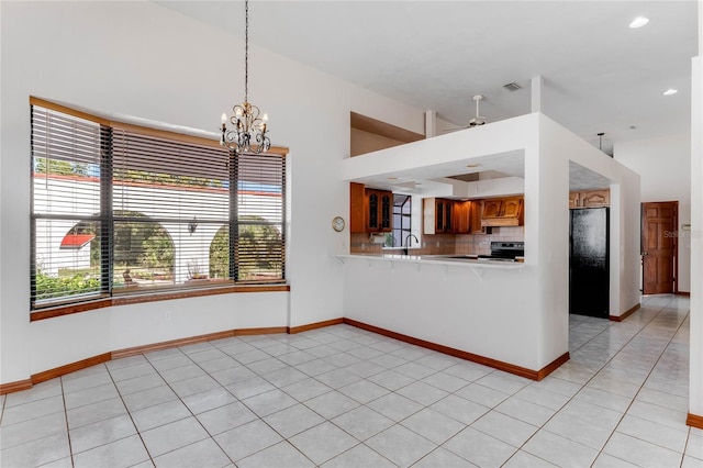 kitchen featuring ceiling fan with notable chandelier, backsplash, kitchen peninsula, pendant lighting, and light tile patterned floors