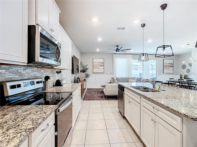 kitchen featuring white cabinets, light stone countertops, decorative light fixtures, stainless steel appliances, and ceiling fan with notable chandelier