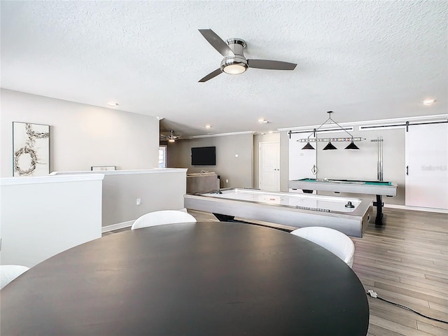 game room with a barn door, a textured ceiling, crown molding, ceiling fan, and hardwood / wood-style flooring