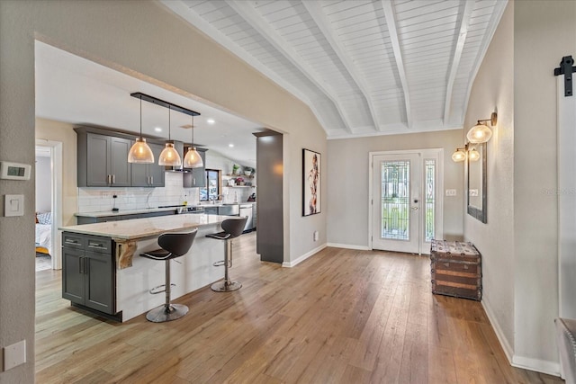 kitchen with light hardwood / wood-style floors, a kitchen island, light stone countertops, pendant lighting, and vaulted ceiling with beams