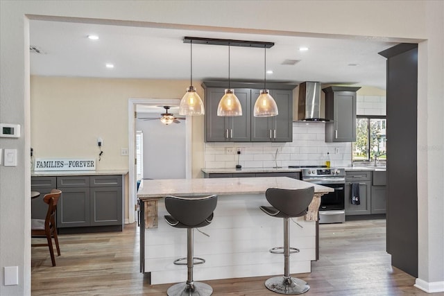 kitchen featuring gray cabinets, stainless steel electric range, decorative light fixtures, and wall chimney range hood