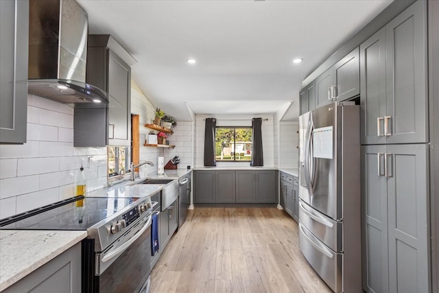 kitchen featuring sink, light hardwood / wood-style flooring, backsplash, wall chimney range hood, and appliances with stainless steel finishes