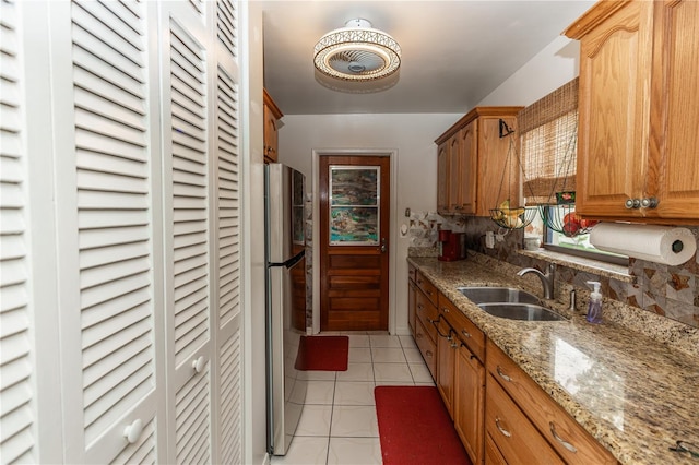 kitchen with stainless steel refrigerator, backsplash, light stone countertops, light tile patterned floors, and sink