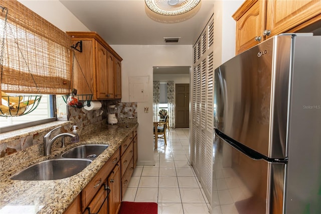 kitchen featuring sink, backsplash, light tile patterned floors, light stone countertops, and stainless steel fridge