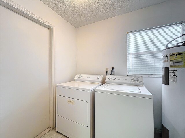 washroom featuring a textured ceiling, water heater, light tile patterned flooring, and washing machine and clothes dryer