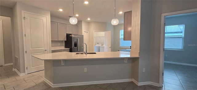 kitchen with independent washer and dryer, a kitchen bar, decorative light fixtures, sink, and stainless steel fridge with ice dispenser