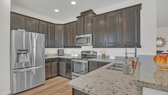 kitchen featuring appliances with stainless steel finishes, light stone counters, light hardwood / wood-style flooring, dark brown cabinetry, and sink