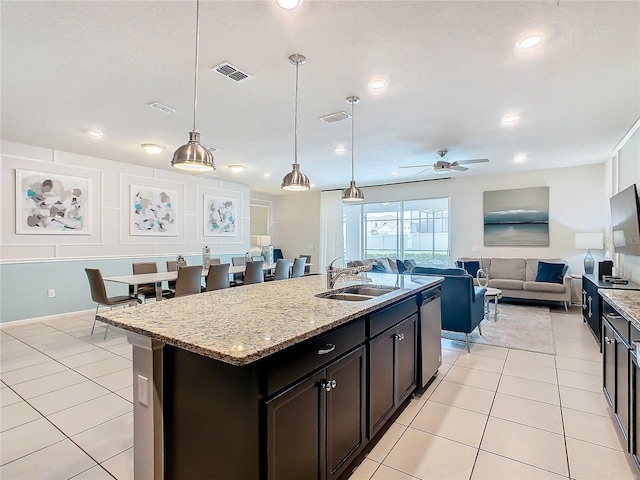 kitchen with ceiling fan, an island with sink, hanging light fixtures, sink, and light stone countertops