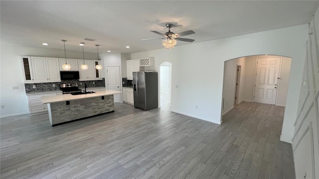 kitchen featuring stainless steel appliances, a kitchen island with sink, pendant lighting, light hardwood / wood-style flooring, and white cabinetry