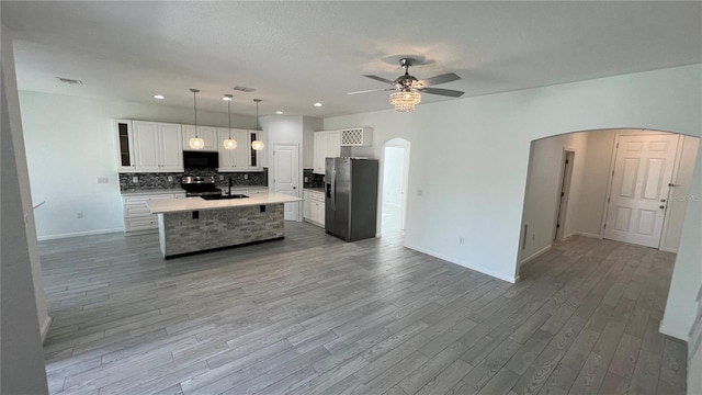 kitchen with appliances with stainless steel finishes, decorative light fixtures, light hardwood / wood-style flooring, white cabinets, and an island with sink