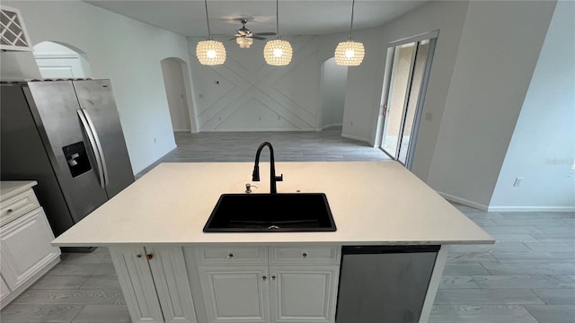 kitchen featuring a center island with sink, white cabinets, sink, hanging light fixtures, and appliances with stainless steel finishes