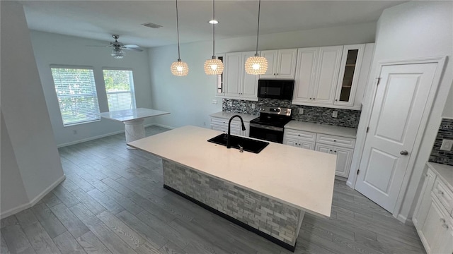 kitchen featuring white cabinetry, ceiling fan, decorative light fixtures, stainless steel electric stove, and a kitchen island with sink