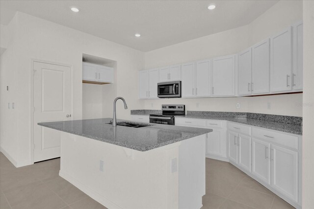 kitchen featuring stainless steel appliances, dark stone counters, a center island with sink, sink, and white cabinets