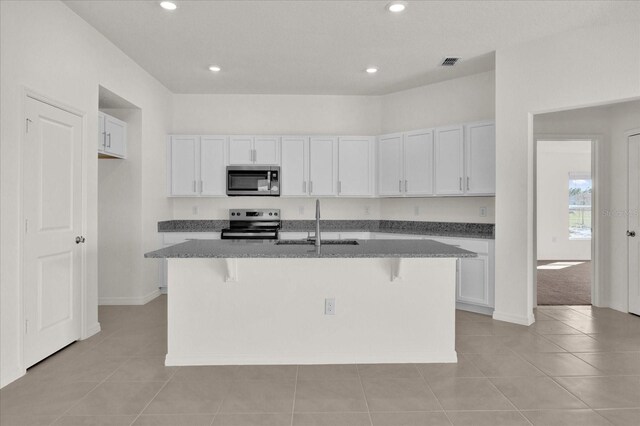 kitchen with sink, appliances with stainless steel finishes, a kitchen island with sink, and white cabinetry