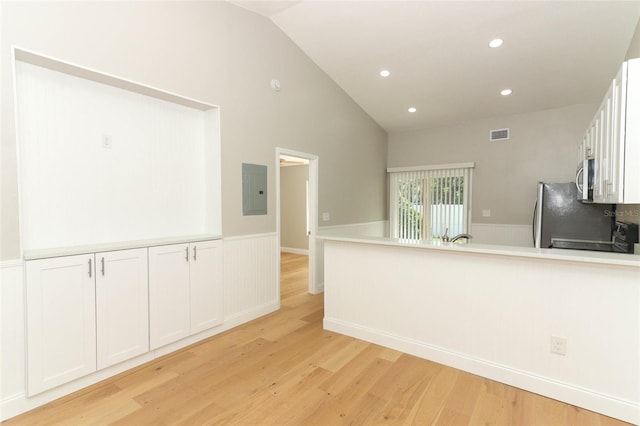 kitchen with light hardwood / wood-style floors, electric panel, white cabinetry, vaulted ceiling, and stainless steel appliances