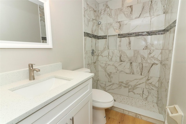 bathroom with wood-type flooring, toilet, vanity, and tiled shower