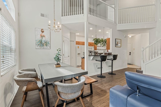 dining space with an inviting chandelier, a towering ceiling, and dark wood-type flooring