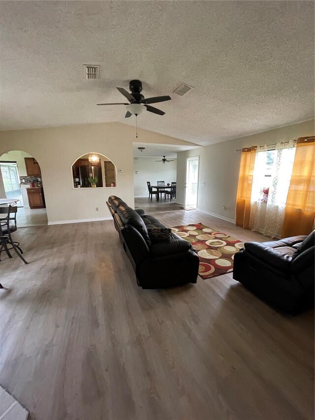 living room with wood-type flooring, lofted ceiling, ceiling fan, and a healthy amount of sunlight