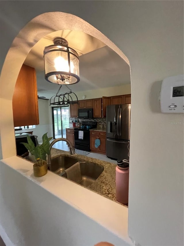 kitchen with a notable chandelier, black appliances, backsplash, and sink