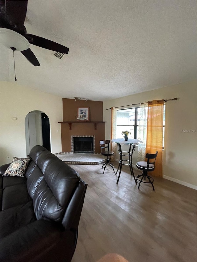 living room featuring a brick fireplace, a textured ceiling, wood-type flooring, and ceiling fan