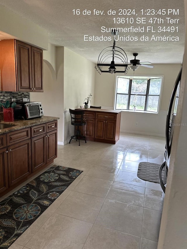 kitchen with a textured ceiling, light tile patterned flooring, tasteful backsplash, hanging light fixtures, and ceiling fan