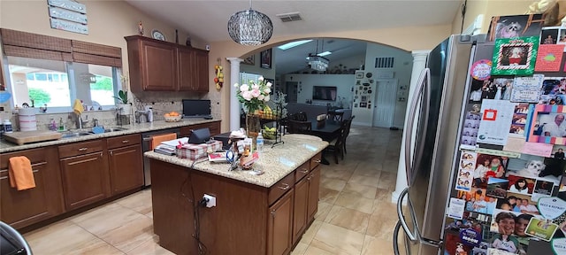 kitchen with ornate columns, stainless steel appliances, vaulted ceiling, pendant lighting, and a center island