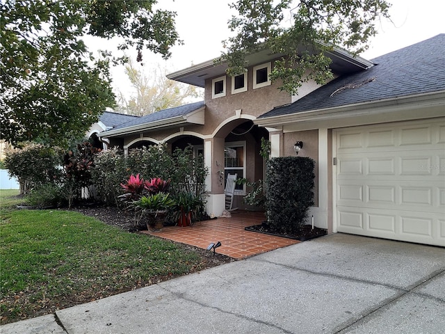 entrance to property with a garage, a shingled roof, a yard, concrete driveway, and stucco siding