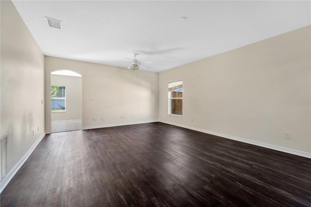 empty room with ceiling fan, a healthy amount of sunlight, and dark wood-type flooring