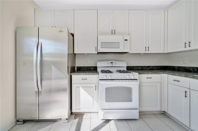 kitchen with white cabinets, dark stone countertops, white appliances, and light tile patterned floors