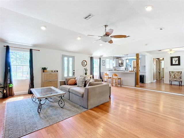 living room with vaulted ceiling, plenty of natural light, ceiling fan, and light wood-type flooring