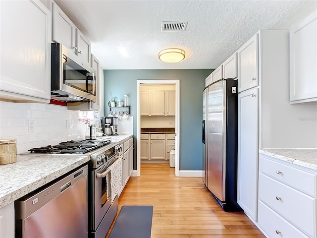 kitchen with appliances with stainless steel finishes, backsplash, white cabinets, light hardwood / wood-style floors, and a textured ceiling