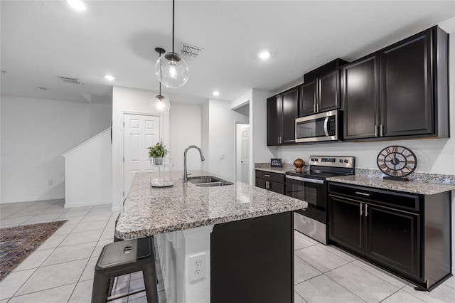 kitchen with an island with sink, a breakfast bar, light tile patterned floors, stainless steel appliances, and sink