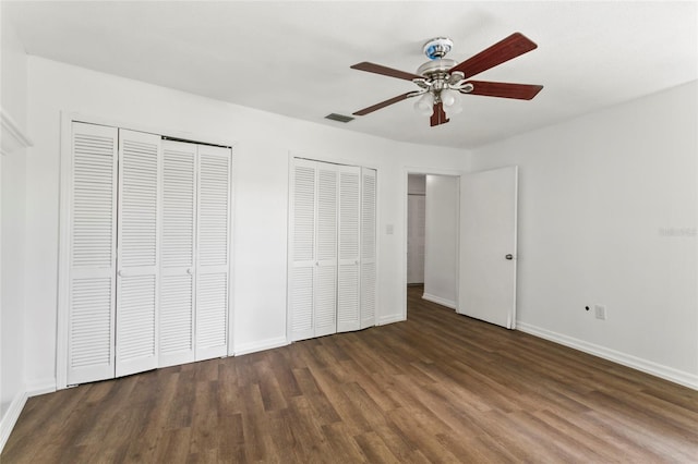 unfurnished bedroom with ceiling fan, multiple closets, and dark hardwood / wood-style floors