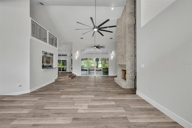 unfurnished living room featuring ceiling fan, a large fireplace, light hardwood / wood-style flooring, and high vaulted ceiling