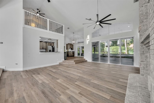 unfurnished living room featuring ceiling fan with notable chandelier, light hardwood / wood-style floors, and high vaulted ceiling