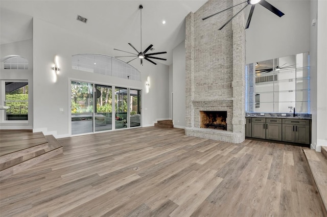 unfurnished living room with high vaulted ceiling, a fireplace, ceiling fan, light hardwood / wood-style flooring, and sink